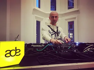 A DJ at a Pioneer DJ setup beside a yellow illuminated ADE sign at Amsterdam Dance Event