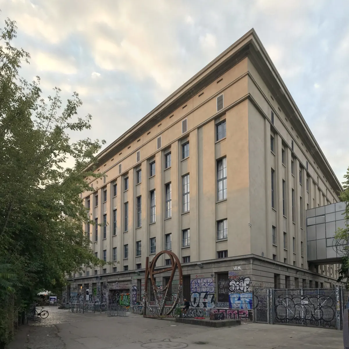 The corner of the Berghain building seen from Am Wriezener Bahnhof, with a rust-coloured sculpture and graffiti at street level