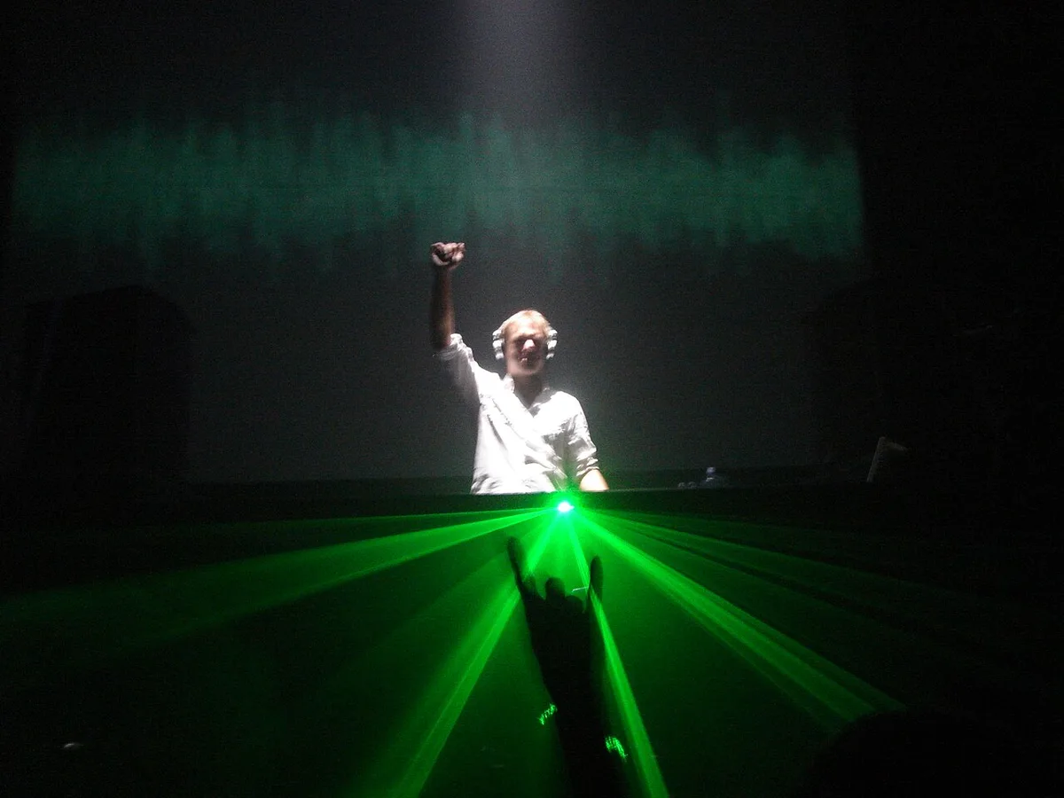 Armin van Buuren with a raised fist behind the decks, green lasers in front of him