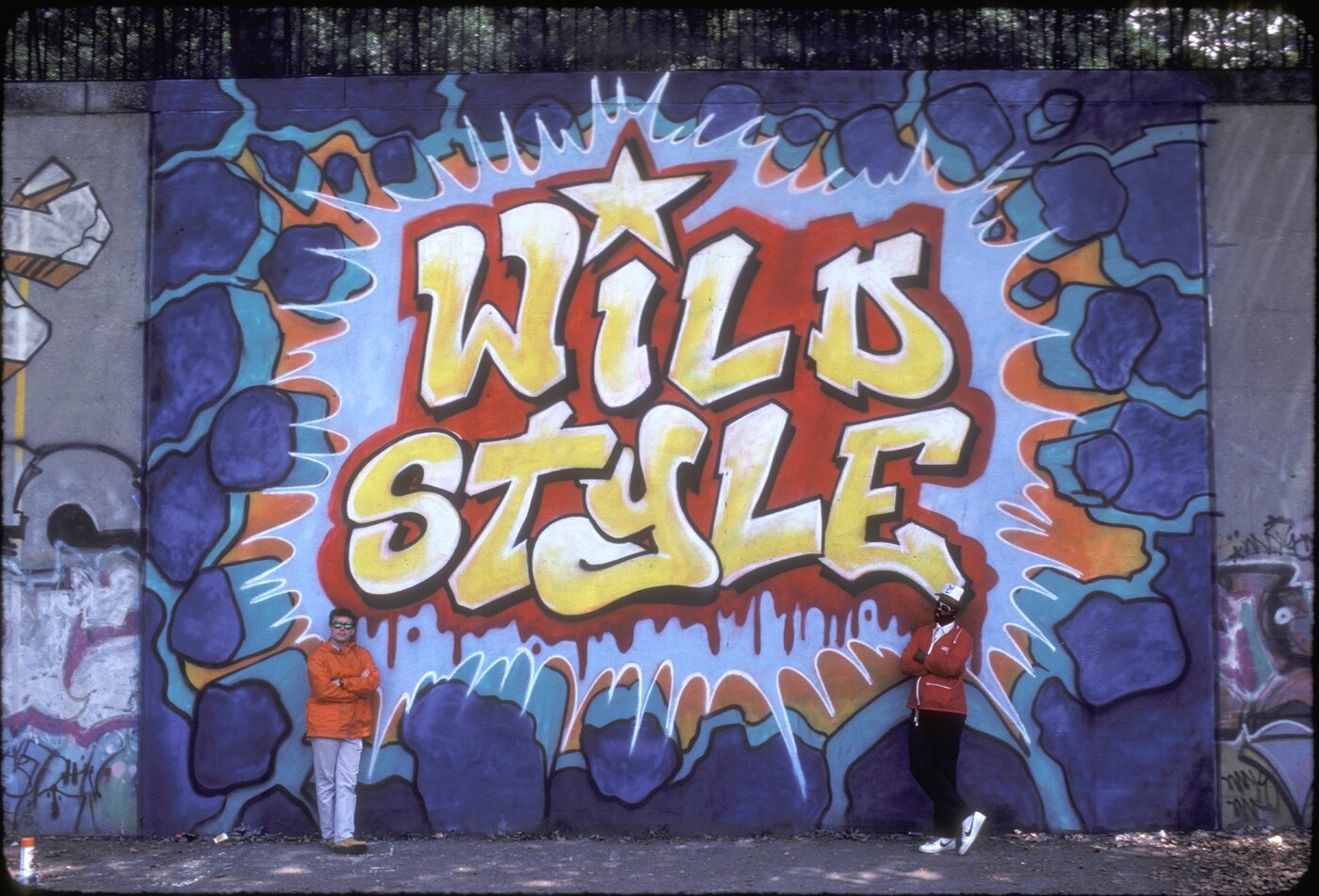 Charlie Ahearn and Fab Five Freddy standing beside the Wild Style mural in 1983