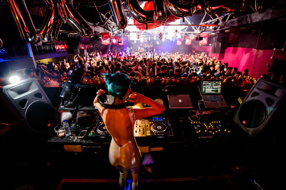 A DJ seen from behind at the decks at Cream in Liverpool, facing a packed dancefloor under balloons