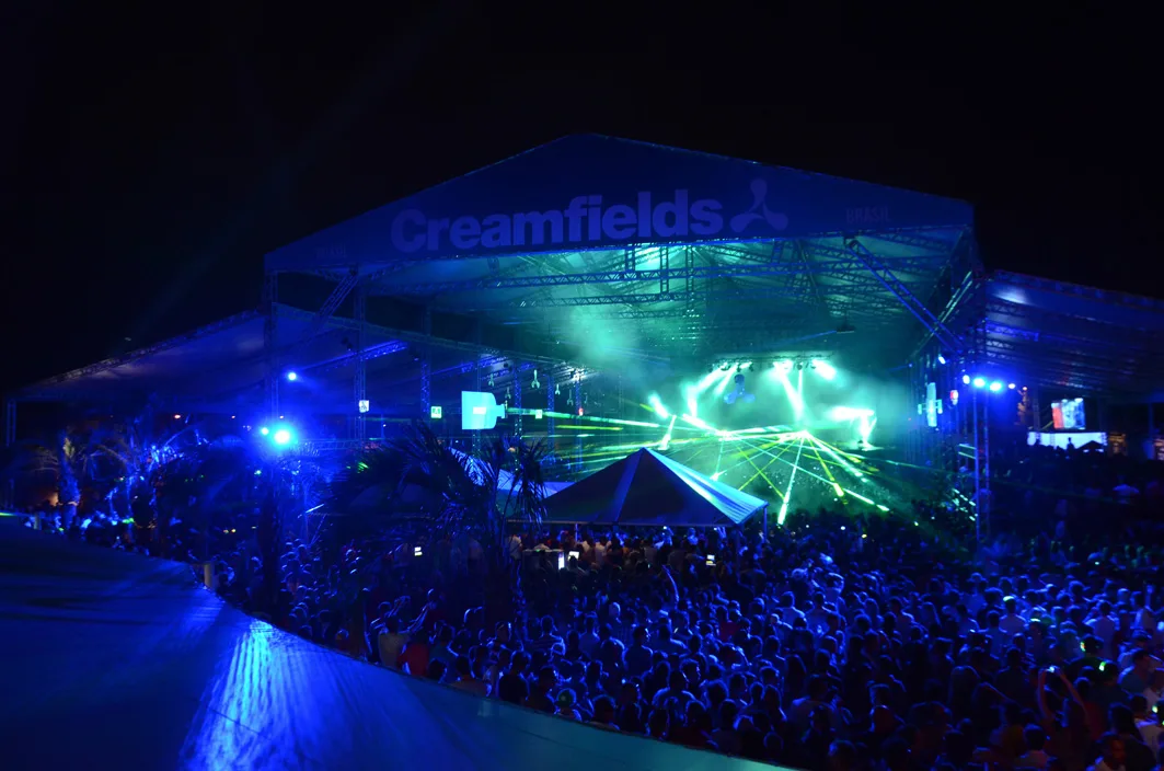 A crowd under a lit Creamfields stage roof at night at Creamfields Brasil in 2013
