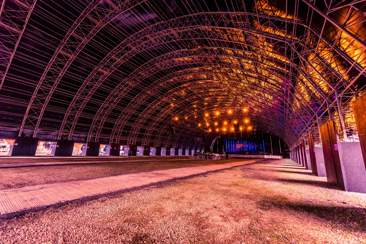 The empty interior of the Steel Yard, a long arched steel structure lit orange, before a show