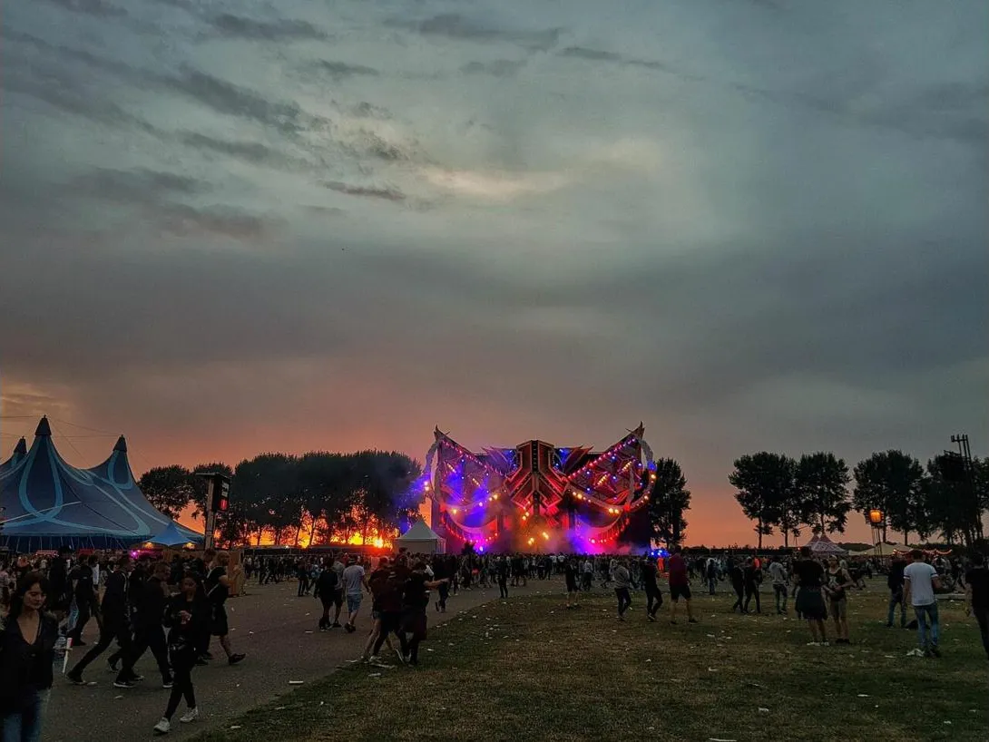 The UV stage at Defqon.1 at sunset, with a crowd walking on the grass
