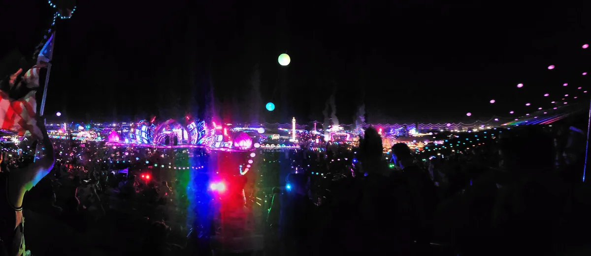 A wide view of the EDC Las Vegas grounds at night, stages and rides lit up inside the speedway