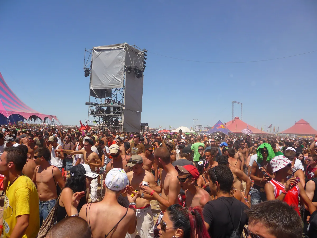 A packed crowd in bright sun at Monegros Desert Festival, with a speaker tower and tents behind