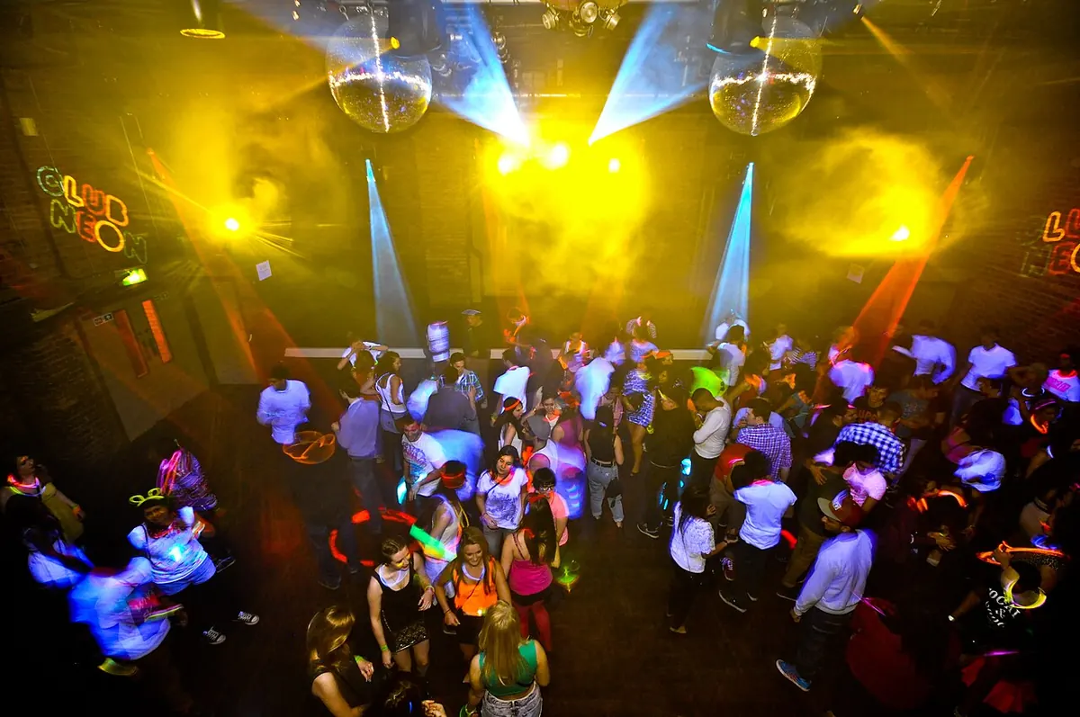Seen from above, a crowd dancing under mirror balls and beams of yellow and blue light at fabric London during a neon party