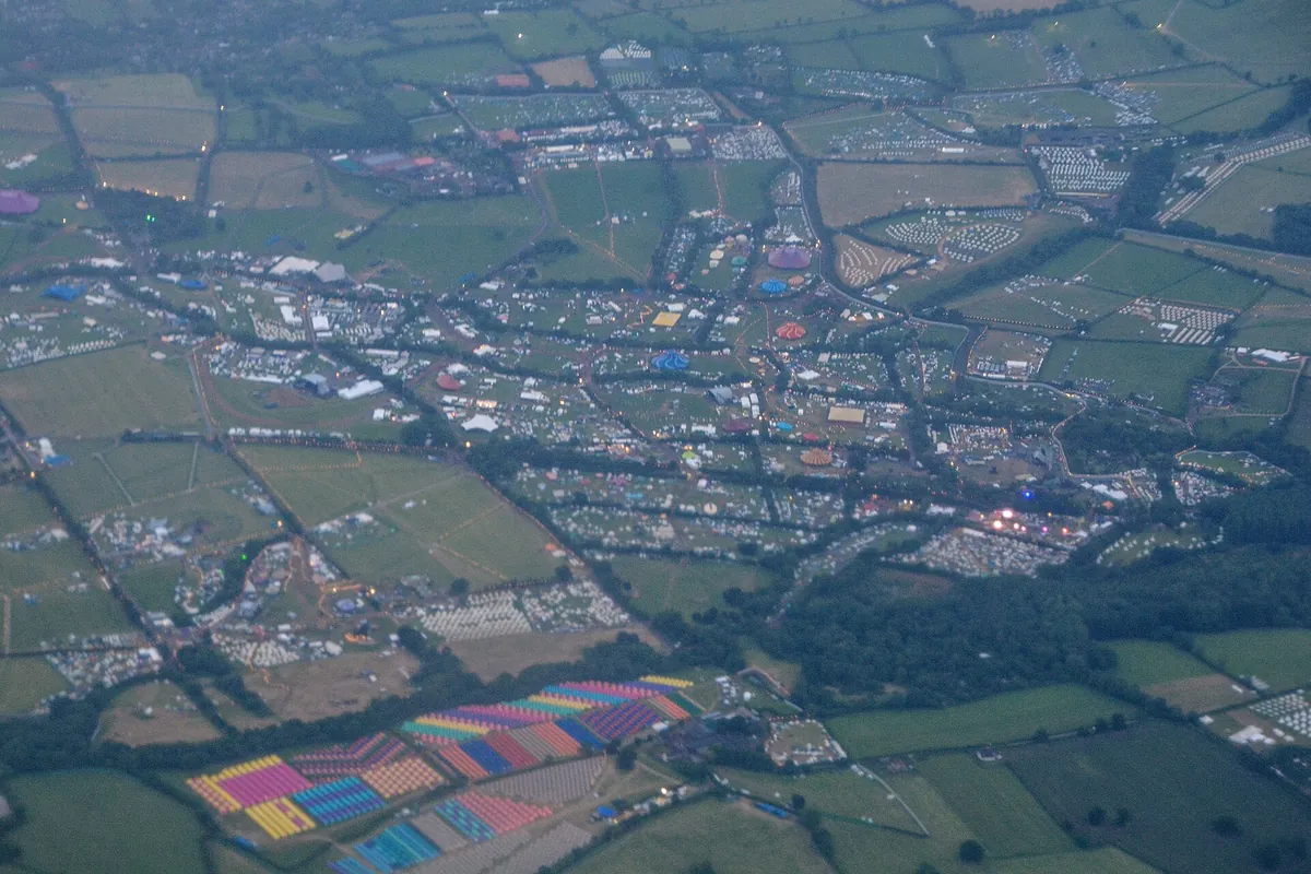 Worthy Farm from the air in June 2022, green fields divided by hedges and filled with tents, marquees and coloured canopies