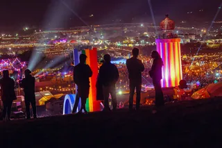 People on a hillside at night looking over the lit stages of Glastonbury in 2025