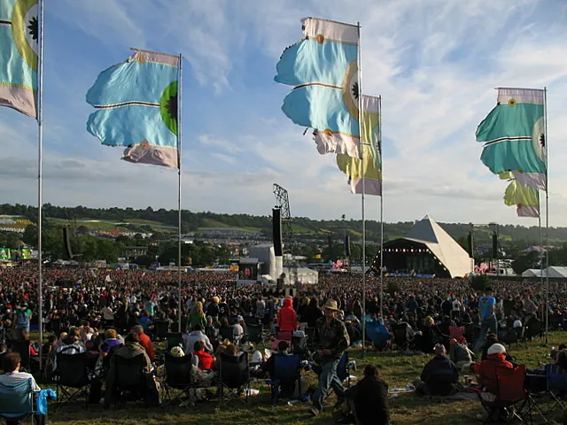 The white Pyramid Stage in the distance on a clear evening in 2008, tall flags and a seated crowd with folding chairs in the foreground