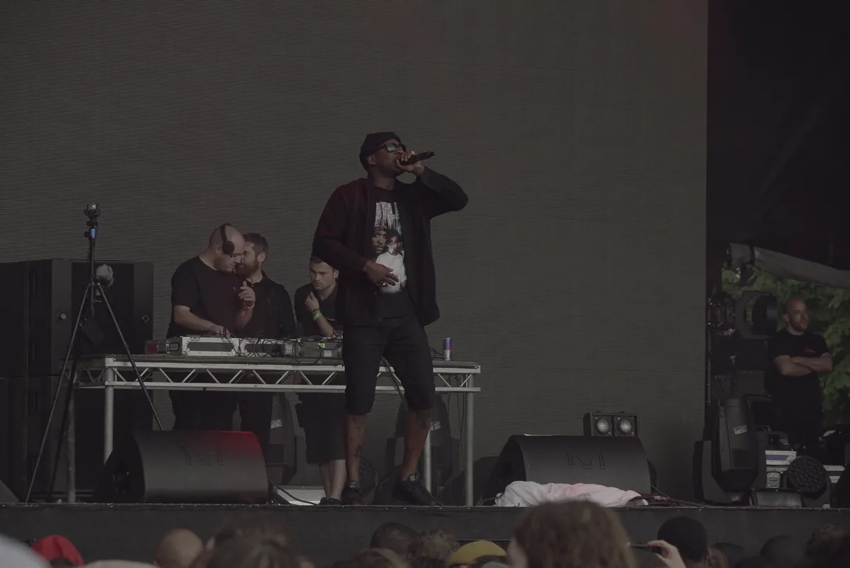Skepta rapping at the front of a festival main stage with DJs behind him
