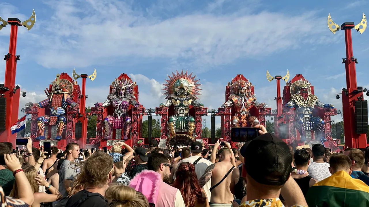 The red main stage at Defqon.1 in 2024, with a large crowd facing the stage in daylight