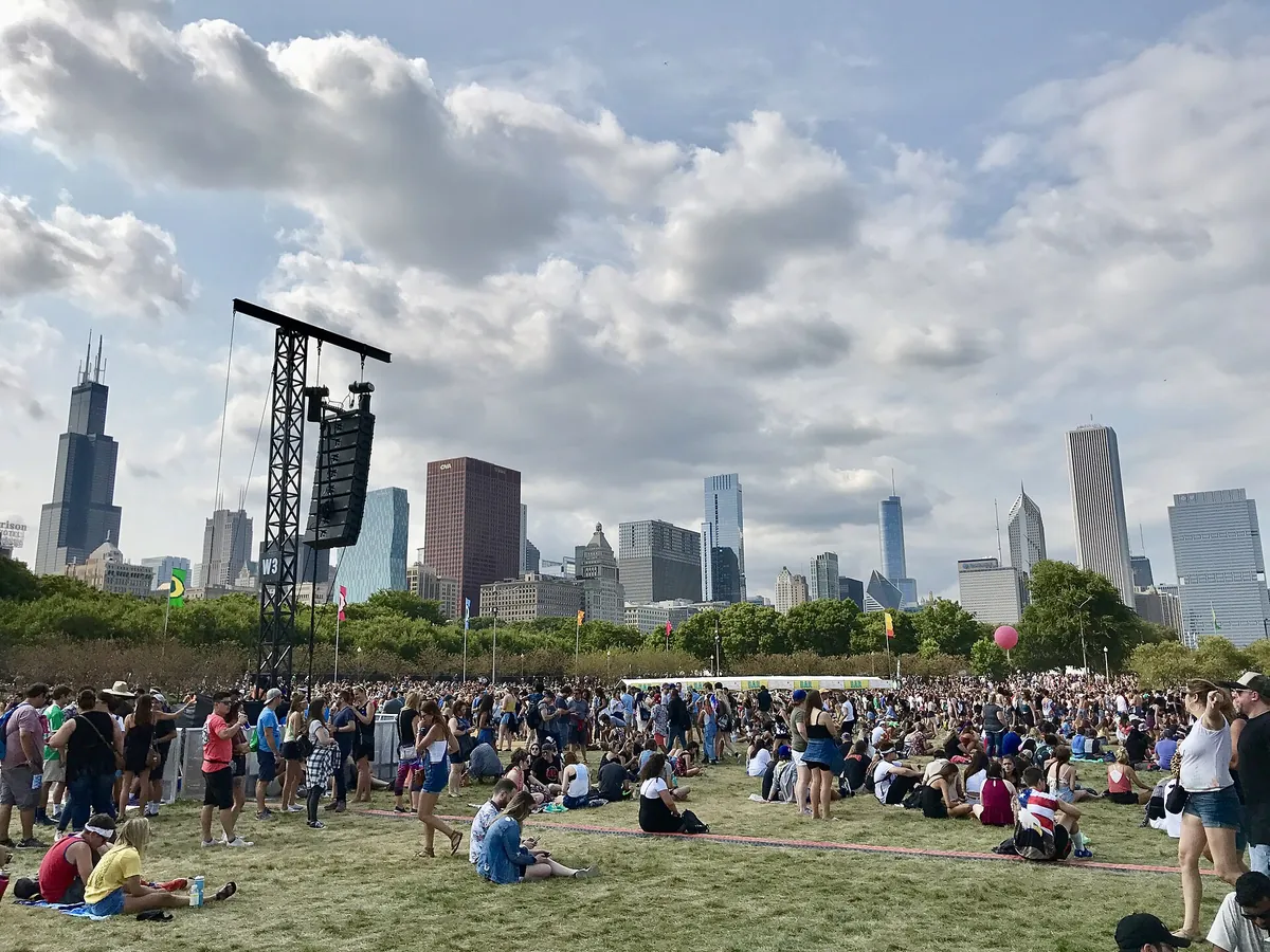 A crowd on the grass in Grant Park during Lollapalooza 2017, a speaker tower to the left and the Chicago skyline behind