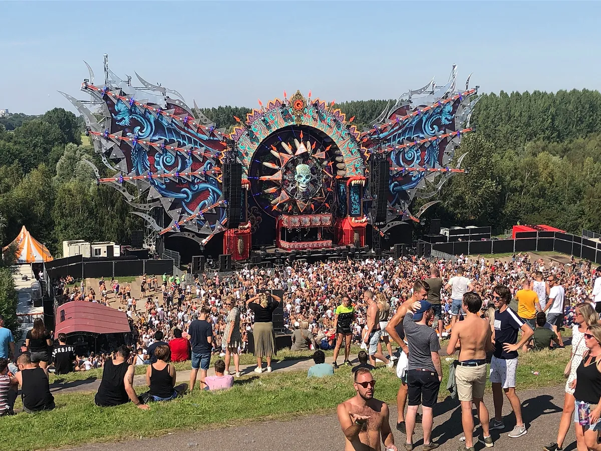 The Q-dance stage at Mysteryland 2019, a winged structure with a skull at its centre, seen from a grassy slope crowded with people