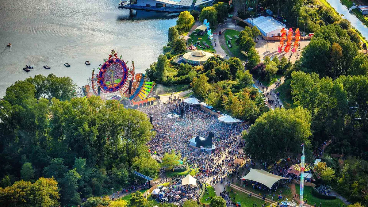 An aerial view of Mysteryland in 2018: a huge decorated main stage on the shore of a lake, a dense crowd in front of it, and woodland, tents and paths around