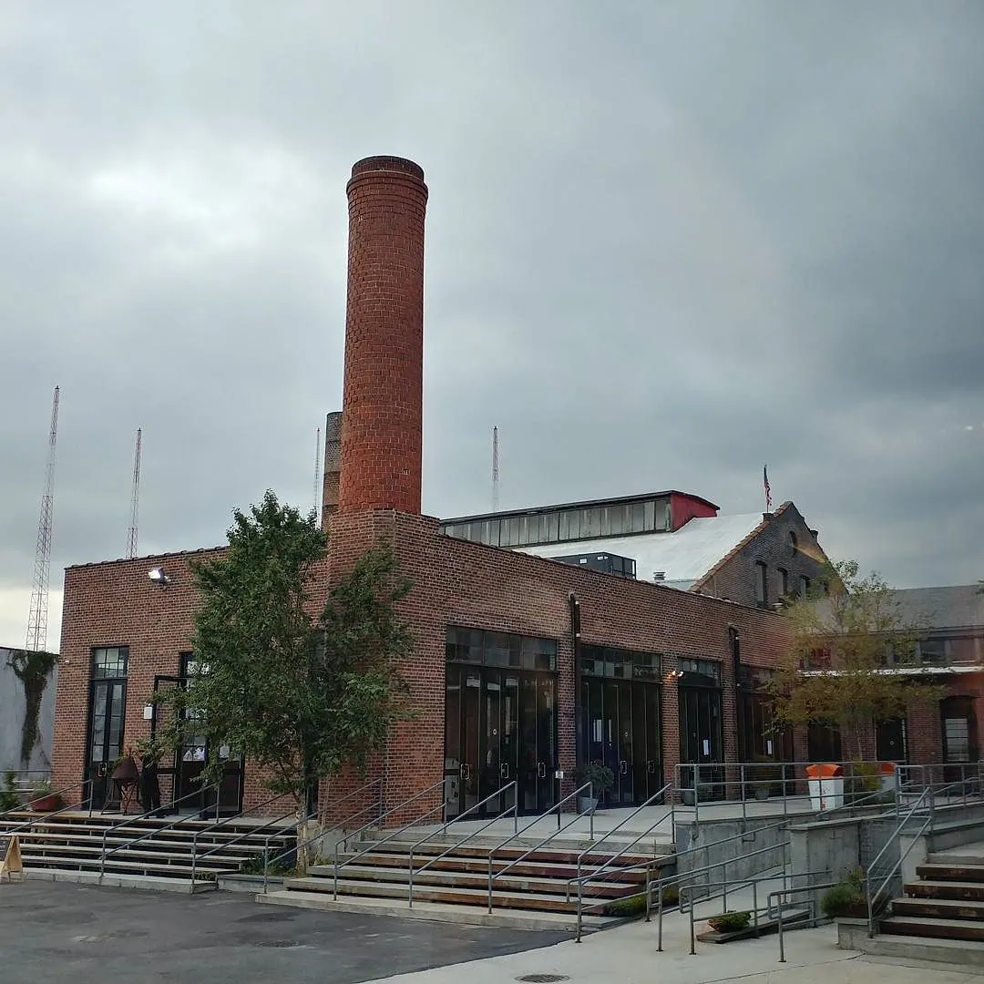 The brick factory buildings and tall chimney of the Knockdown Center in Maspeth under a grey sky