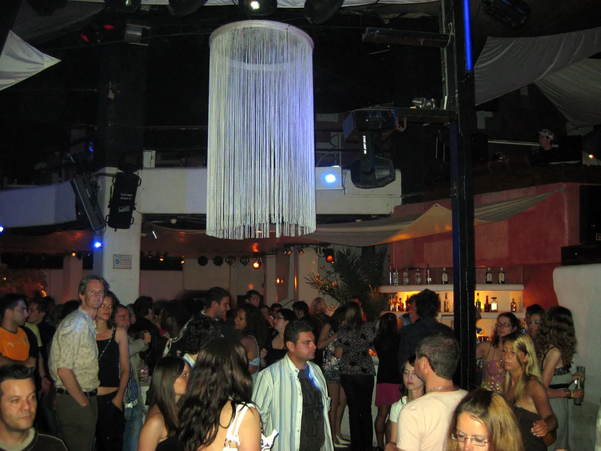 A crowd dancing on the Main Room floor at Pacha Ibiza under a large white fringed lamp