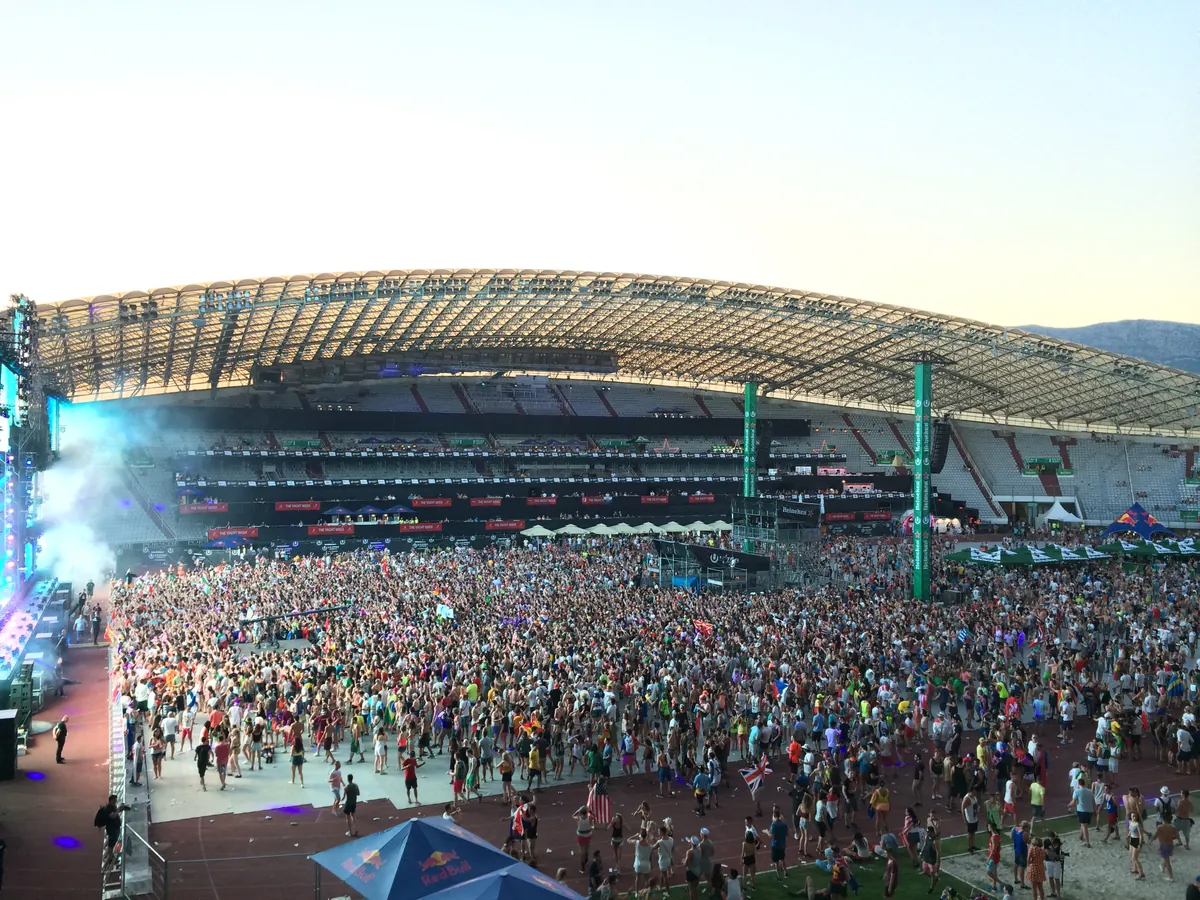A daytime crowd on the pitch of the Poljud Stadium in Split during Ultra Europe 2015, under the stadium's arched roof