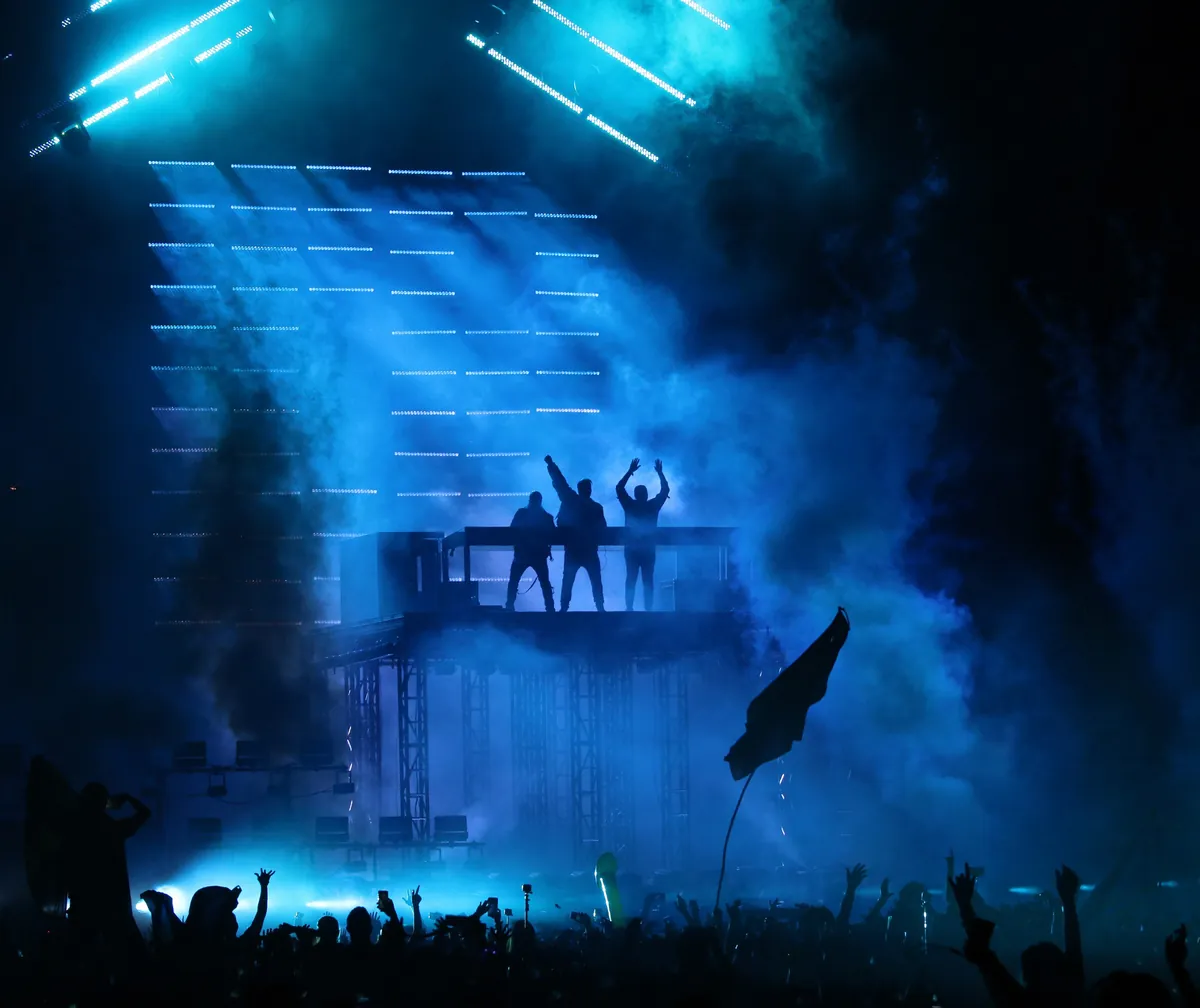 Swedish House Mafia silhouetted on a raised platform in blue light and smoke above the crowd at Ultra Miami 2018