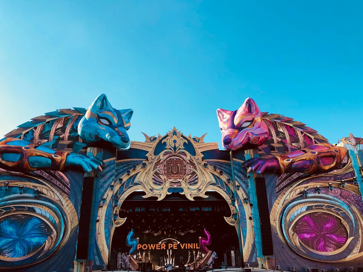 The top of the Untold main stage in 2018, two giant painted wolf heads, one blue and one pink, reaching over an ornate gold arch against a clear sky